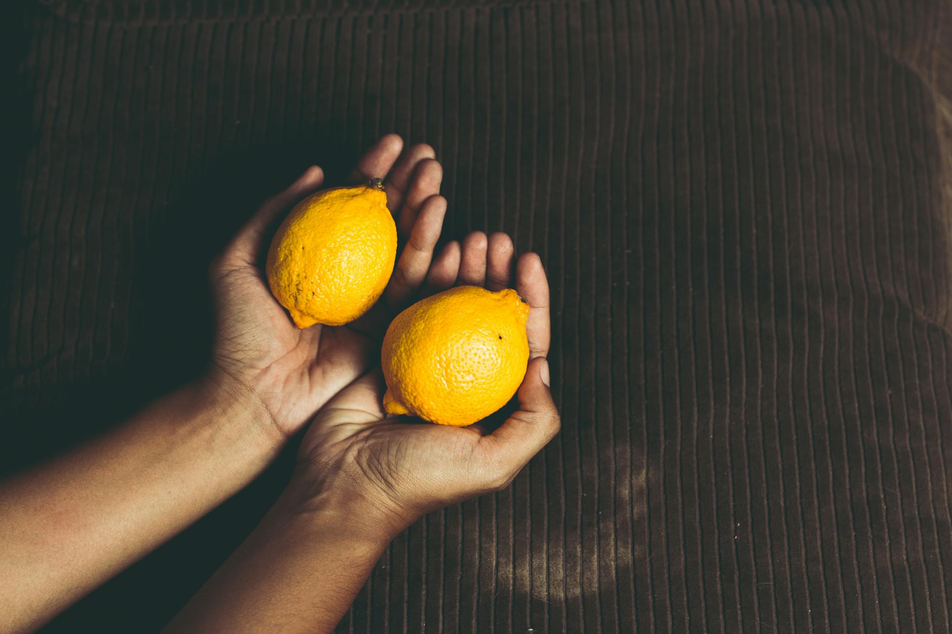Gros plan de citrons frais tenus dans les mains en coupe sur une surface marron