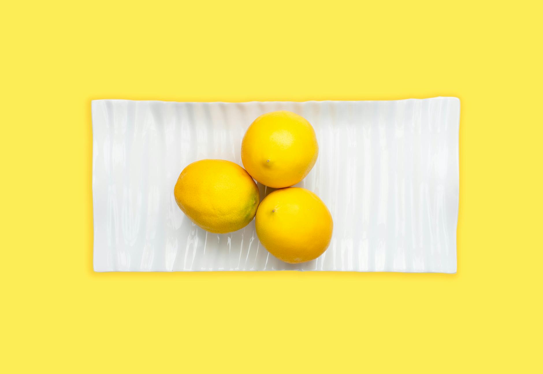 Trois citrons frais arrangés sur une assiette blanche avec un fond jaune vibrant