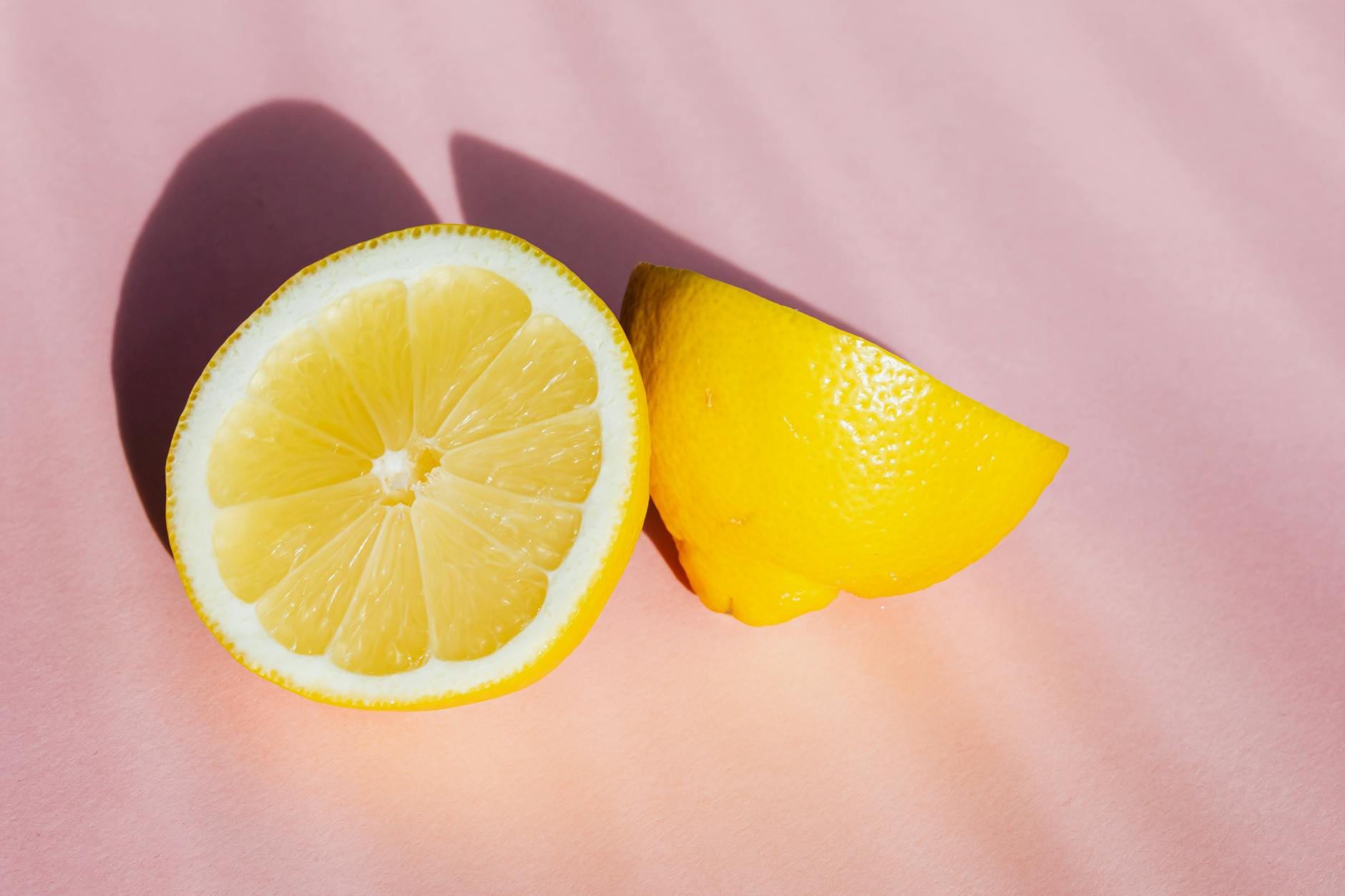 Citrons frais coupés en deux sur fond rose avec rayons de soleil