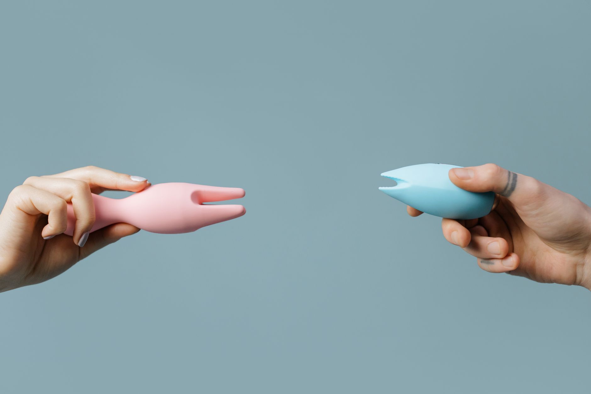 Deux mains tenant des vibromasseurs rose et bleu sur fond pastel, symbole de plaisir partagé