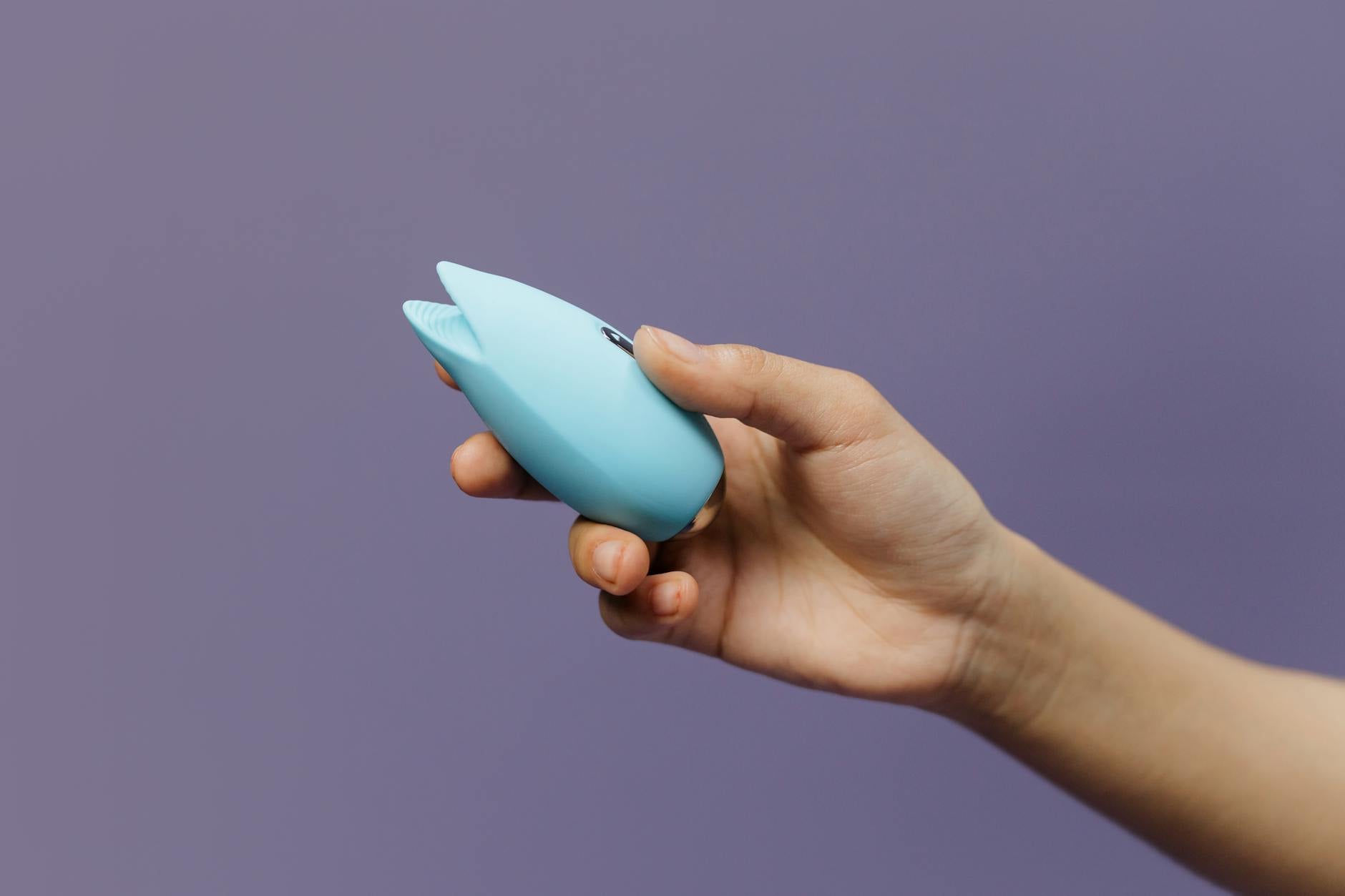 A blue silicone vibrator held in hand against a purple background, demonstrating modern pleasure tools for midlife
