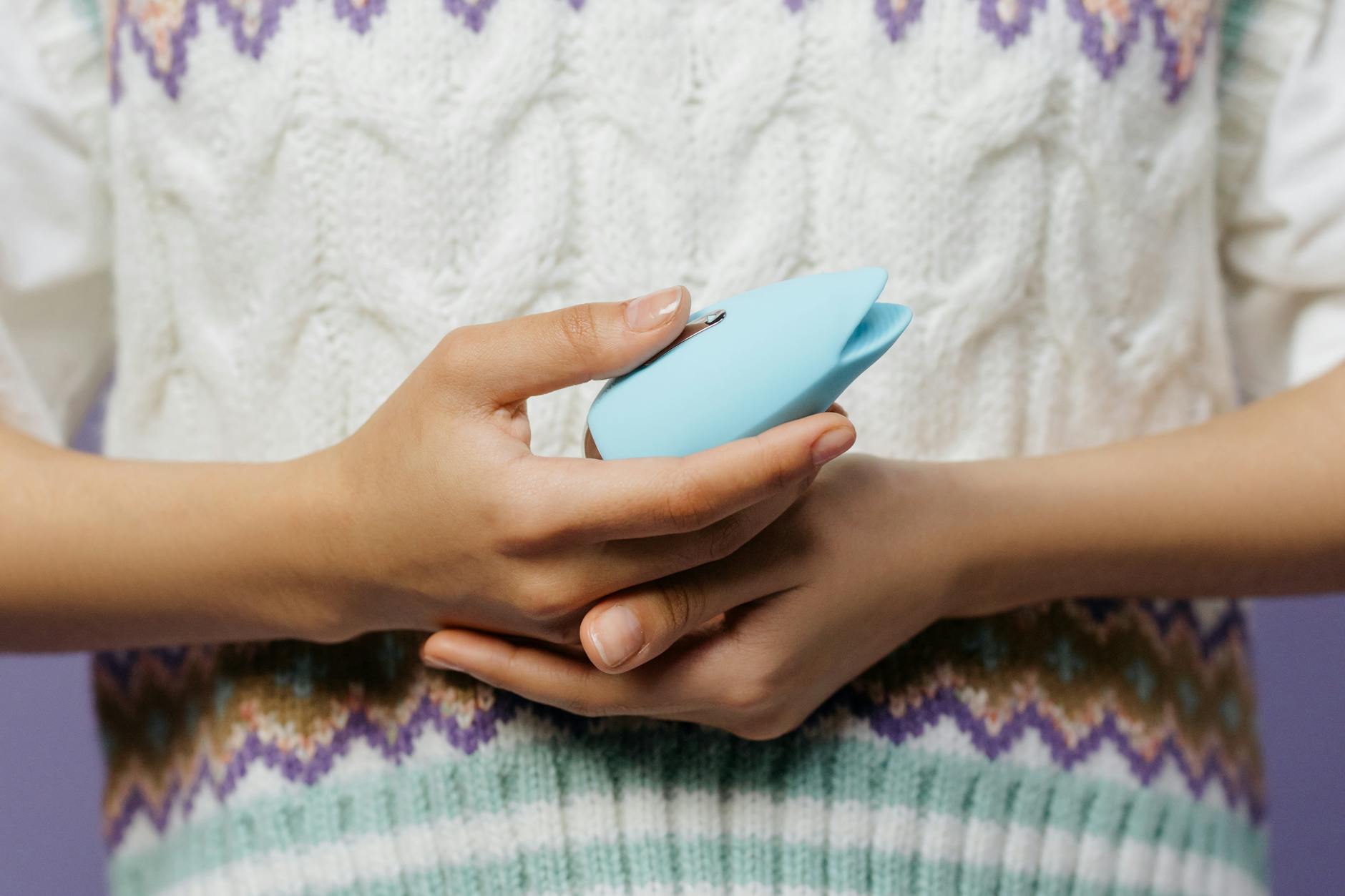 Close-up of a hand holding a lemon clitoral vibrator against a knitted sweater