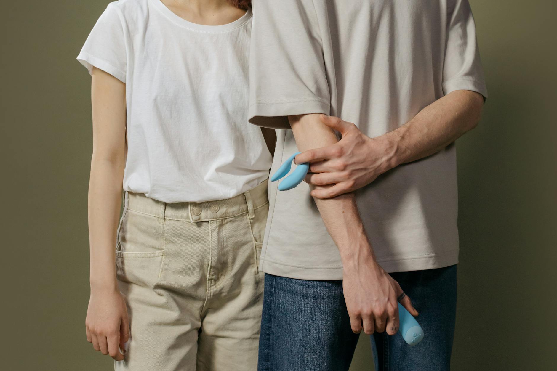 Un jeune couple enlacé tenant ensemble un vibromasseur bleu, symbolisant l'intimité moderne et la reconnexion.